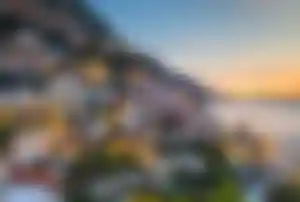 Bunte Häuser an einem steilen Küstenhang der Amalfiküste in Italien bei Sonnenuntergang mit Blick auf das Mittelmeer.