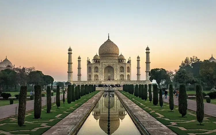 Taj Mahal im Sonnenaufgang mit Spiegelung im Wasserbecken und symmetrischen Gärten