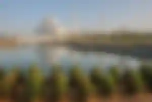 Große weiße Moschee mit Kuppeln und Minaretten, spiegelndes Wasserbecken im Vordergrund und gepflegte Gartenanlage