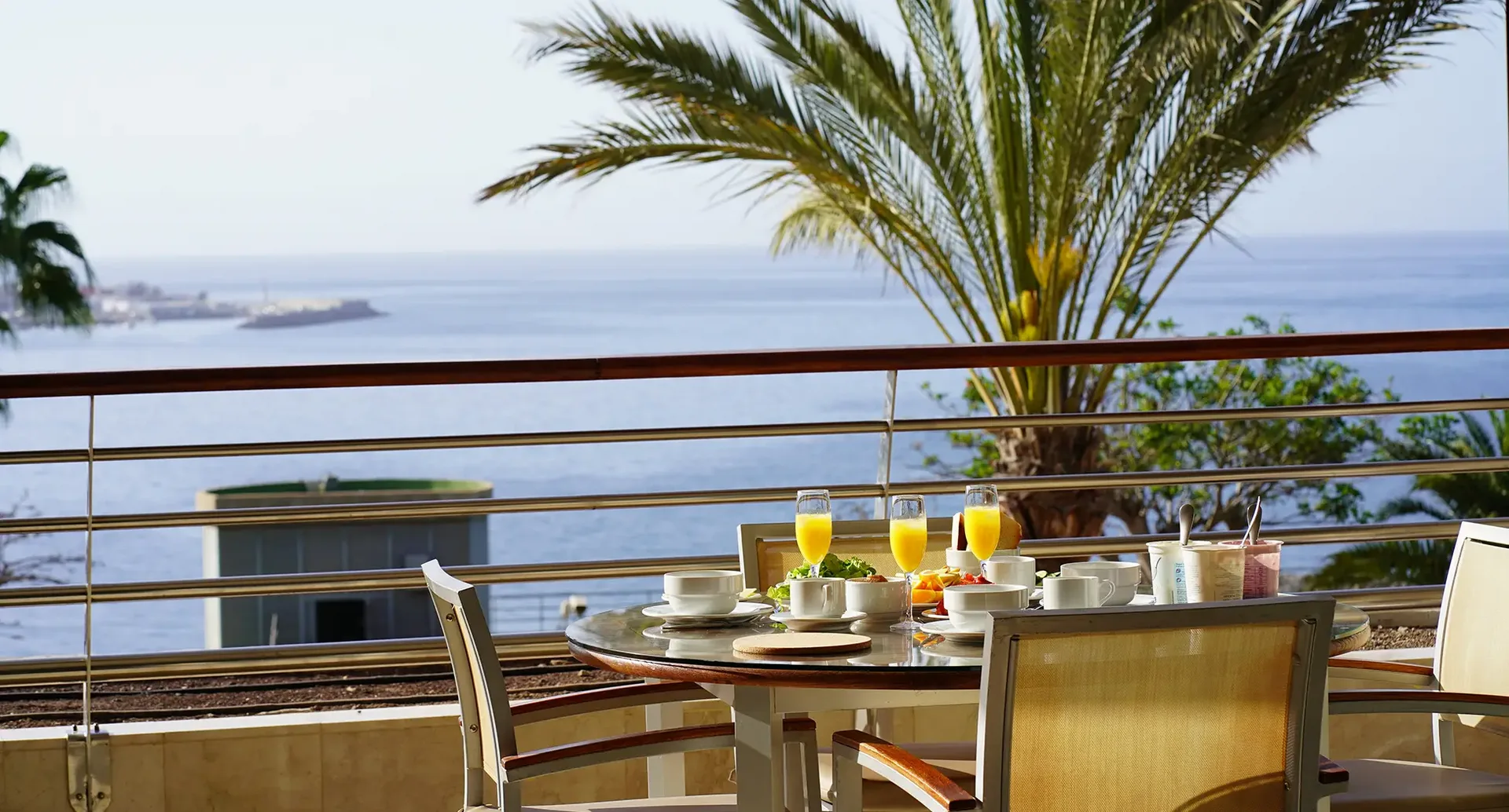Terrasse mit Meerblick – Frühstück im Spanien Urlaub Frühstückstisch auf einer Terrasse mit Blick auf das Meer und Palmen in einer spanischen Urlaubsregion.