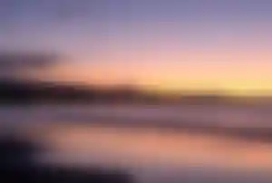 Strandansicht auf Gran Canaria bei Sonnenuntergang mit ruhigem Meer und beleuchteter Küstenlinie Bildtitel: