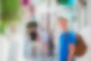 Alleinreisende Person erkundet die weißen Gassen von Mykonos mit Rucksack und Sonnenhut