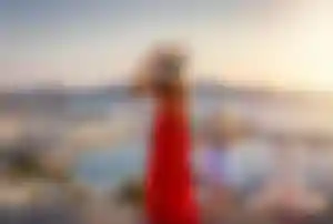 Erwachsene Person und Kind mit Sonnenhüten genießen den Ausblick auf die Küste und die weißen Häuser einer griechischen Insel