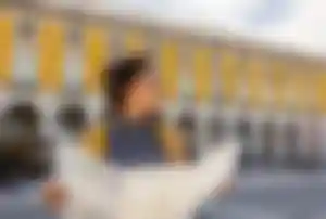 Person steht auf einem Platz vor einem gelben historischen Gebäude und hält eine aufgefaltete Stadtkarte in den Händen