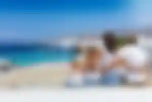 Familie sitzt auf einer Terrasse mit Blick auf das Meer, weiße Häuser und die Küste einer griechischen Insel