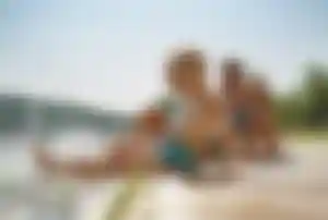 Mehrere Personen sitzen auf einem Holzsteg am See, ein Kind lässt die Beine ins Wasser und spritzt, während die anderen daneben sitzen.