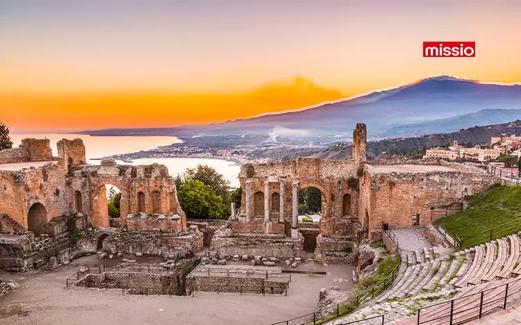 Antikes griechisches Theater von Taormina mit Blick auf die sichelförmige Küste und den Ätna bei farbigem Sonnenuntergang