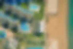 Luftaufnahme einer weitläufigen Clubanlage direkt am Sandstrand mit mehreren Pools, Wasserrutschen, gepflegten Grünflächen und Strandliegen an der türkischen Riviera.