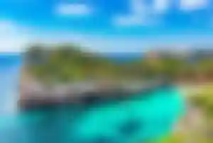 Felsige Badebucht mit türkisblauem Wasser, Pinien, Klippen und kleinem Boot vor der Küste Mallorcas