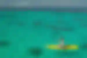 Stand-up-Paddling im klaren Meer als entspannter Urlaubsmoment Person sitzt auf einem gelben Stand-up-Paddleboard und paddelt auf klarem, türkisfarbenem Meer