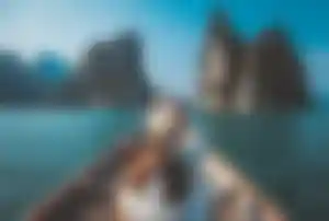 Person sitzt in einem Holzboot auf dem Meer und blickt in Richtung hoher Felseninseln in einer tropischen Küstenlandschaft