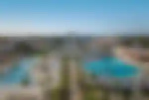 Große Resortanlage mit mehreren Pools, palmengesäumten Wegen, Liegen und Gebäuden im mediterranen Stil an der türkischen Mittelmeerküste.