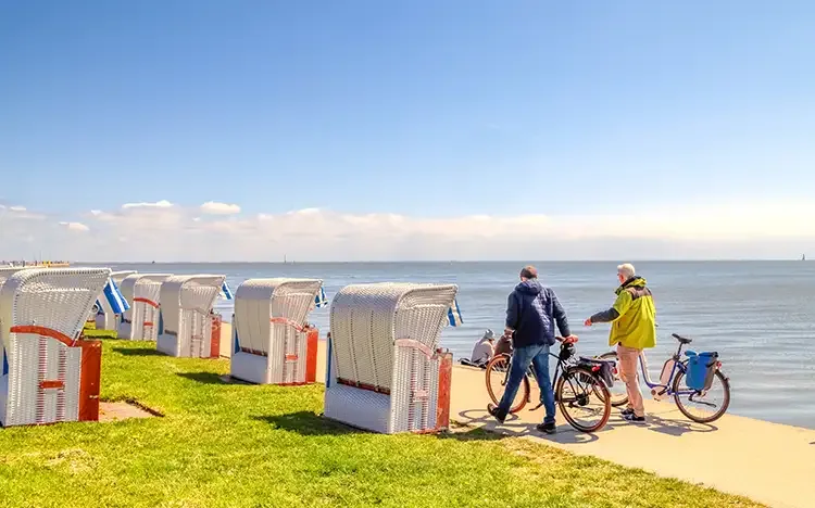 Strandpromenade mit Strandkörben und zwei Personen mit Fahrrädern am Wasser in Wilhelmshaven.