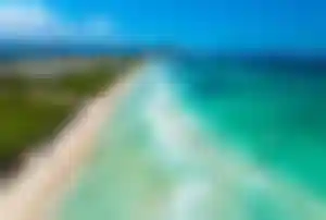 Luftaufnahme der Playa de Muro auf Mallorca mit langem Sandstrand, türkisblauem Wasser, sanften Wellen und Hotelanlagen entlang der Küste.