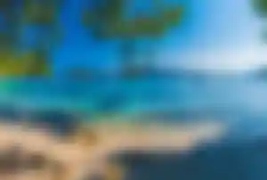 Strand der Playa de Formentor auf Mallorca mit kristallklarem Wasser, Pinienbäumen, kleinen Booten und Bergen im Hintergrund.