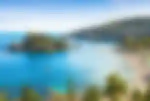 Malerische Bucht auf Sizilien mit türkisblauem Meer, kleinen Inseln, Sandstrand und felsiger Küstenlandschaft.