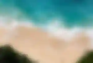 Traumstrand mit türkisfarbenem Wasser Türkisblaues Meer mit Wellen trifft auf einen hellen Sandstrand, aufgenommen aus der Vogelperspektive mit wenigen Menschen am Ufer