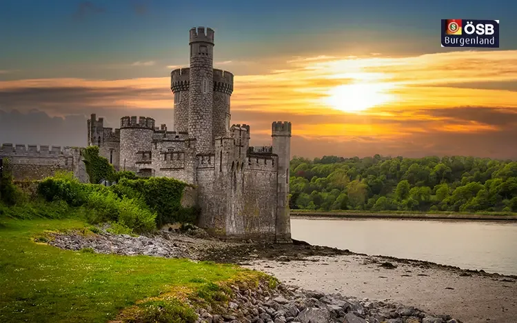 Historisches Schloss in Cork am Wasser bei Sonnenuntergang mit bewaldeter Umgebung.