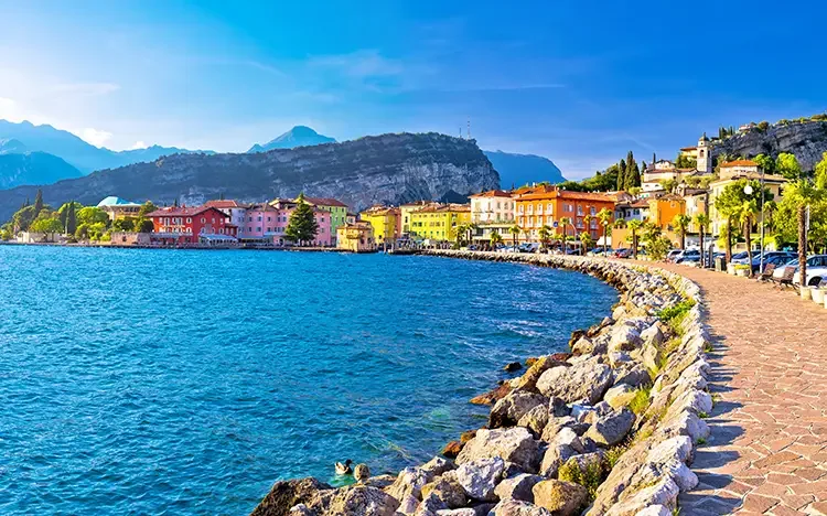 Promenade von Torbole am Gardasee mit bunten Häusern, Uferweg und Blick auf den See und die Berge