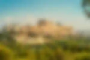 Akropolis in Athen mit dem Parthenon-Tempel auf einem Hügel, umgeben von grüner Landschaft und antiken Ruinen