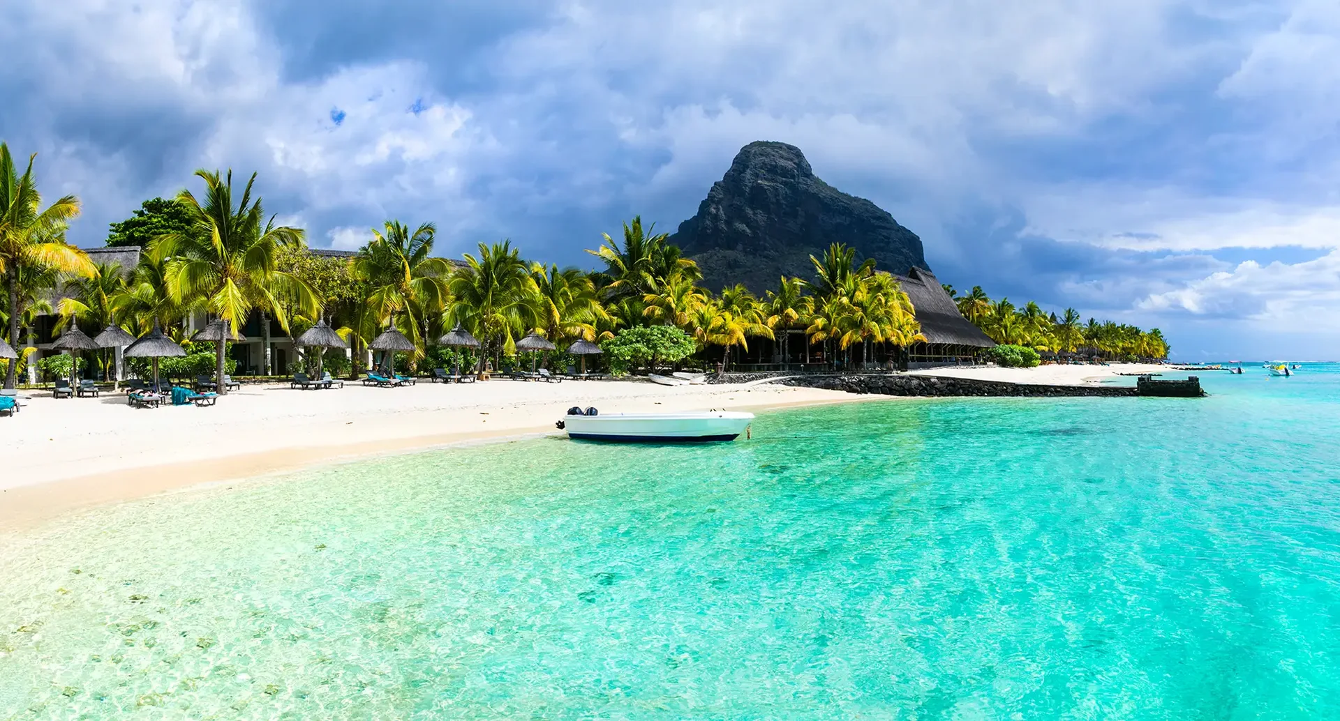 Traumstrand auf Mauritius mit klaren Lagunen, Palmen und Blick auf einen markanten Berg am Horizont.
