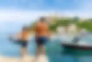 Erwachsene Person und Kind stehen an einem Hafen in Kroatien und blicken auf Boote und eine Küstenstadt am Meer.