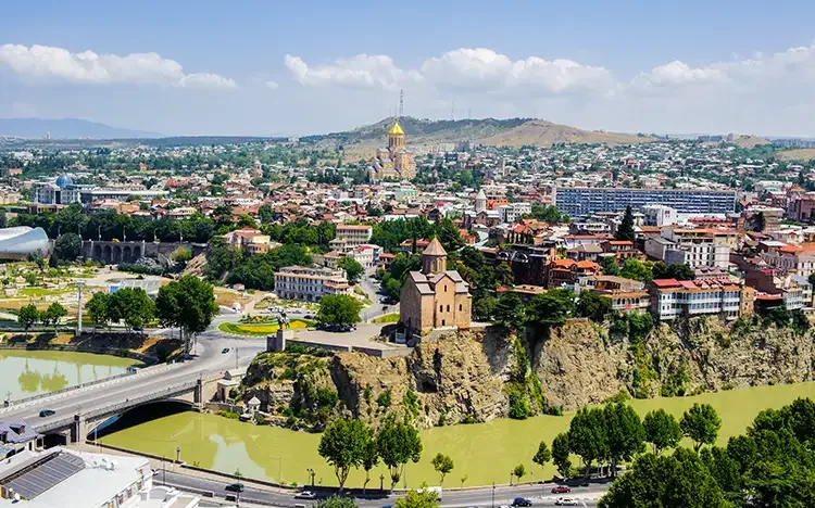 Panoramablick über Tiflis, mit der Metekhi-Kirche auf einer Klippe, dem Fluss Kura und der Stadt im Hintergrund.
