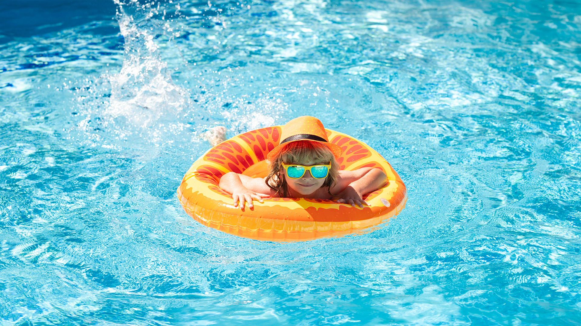 Kind mit Sonnenhut und Schwimmreifen in einem Hotelpool während eines Sommerurlaubs mit Kindern