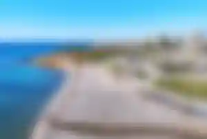 Breiter Strand mit hellen Kieselsteinen und Promenade an der Costa Blanca in Spanien.