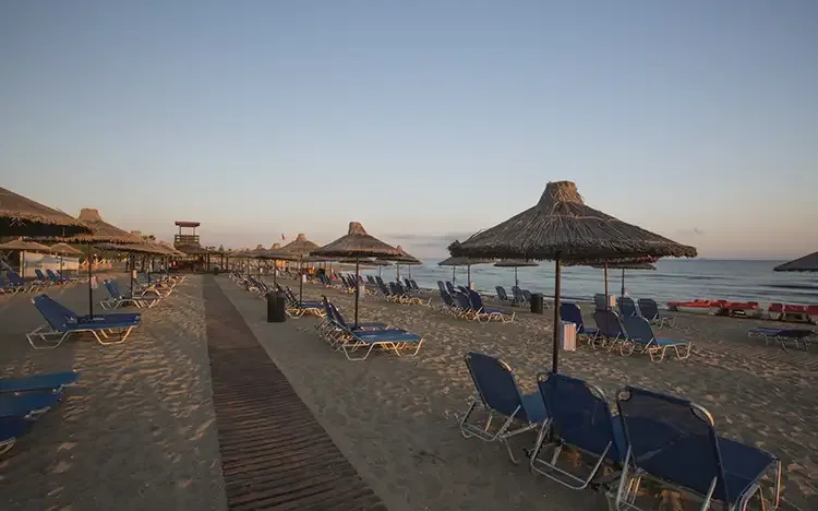 Sandstrand mit Sonnenliegen und Strohdächern bei Sonnenuntergang auf Kreta.