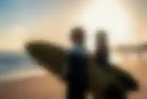 Zwei Personen mit Surfboards am Strand bei Sonnenuntergang