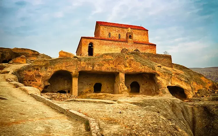 Die antike Höhlenstadt Uplistsikhe in Georgien mit in Fels gehauenen Räumen und einer alten Kirche darüber.