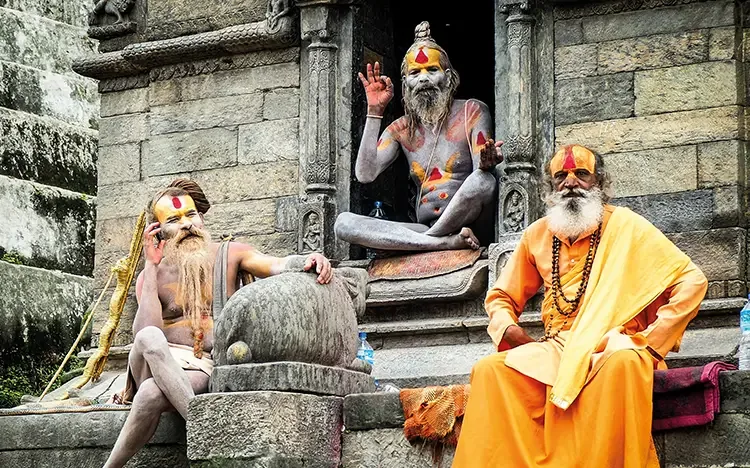 Drei spirituelle Männer mit bemalten Körpern sitzen vor einem steinernen Tempel und posieren