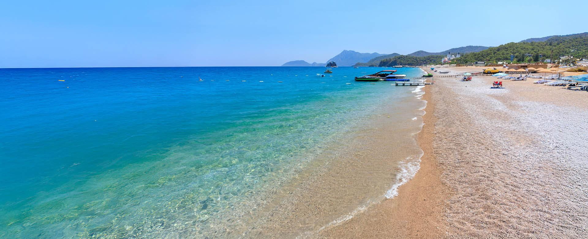 Türkische Riviera Urlaub Strand an der türkischen Riviera bei Kemer mit klarem Wasser, Booten und Bergen im Hintergrund