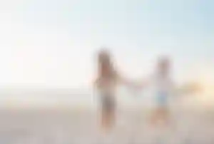 Drei Personen spazieren gemeinsam an einem breiten Sandstrand entlang der Küste