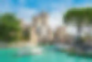 Burganlage von Sirmione am Gardasee mit türkisfarbenem Wasser, kleinen Booten und mediterraner Uferlandschaft.