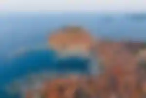 Luftaufnahme der Altstadt von Rovinj auf einer Halbinsel mit dicht bebauten Häusern, Kirchturm, Hafenanlage und Booten im glasklaren Wasser der Adria entlang der Küste.