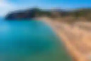Tsambika Beach auf Rhodos mit langem Sandstrand, türkisblauem Wasser und bewaldeten Hügeln im Hintergrund