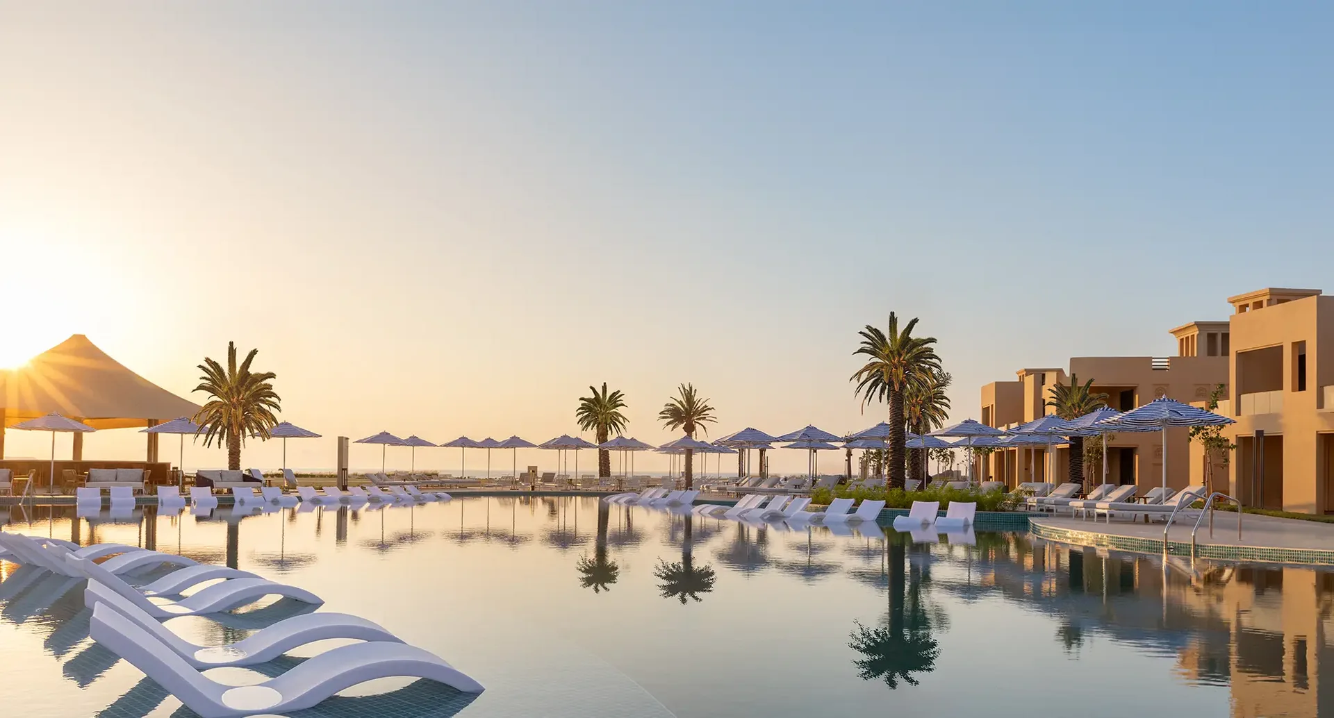 Luxuriöse Poolanlage eines 5-Sterne-Strandresorts in Dubai bei Sonnenuntergang mit Palmen, Liegen und entspannter Urlaubsatmosphäre