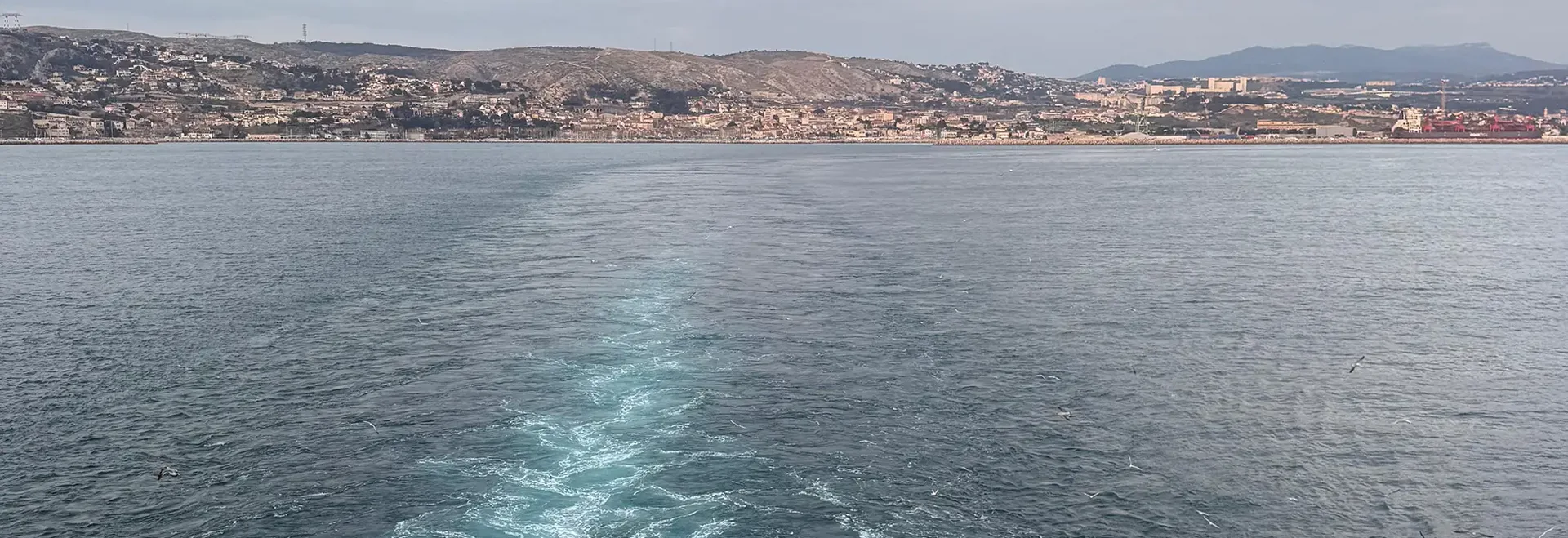 Ausblick auf die Küste vom Kreuzfahrtschiff Meerblick vom Schiff aus mit sichtbarer Heckwelle und Blick auf Küstenlandschaft