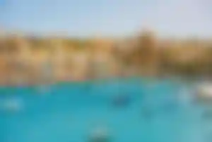 Hafen von Valletta in Malta mit türkisblauem Wasser, vielen kleinen Booten und historischer Stadt mit Kuppelkirche im Hintergrund