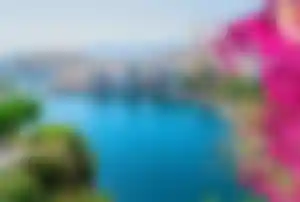 Hafen von Agios Nikolaos mit türkisblauem Wasser, Booten, Promenade und blühenden Bougainvillea an der Küste Kretas