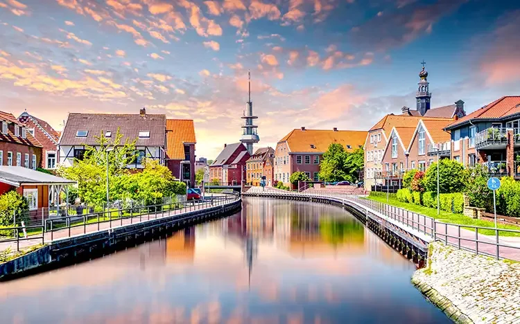 Blick auf den Kanal in Emden mit historischen Häusern und Kirche bei Sonnenuntergang.