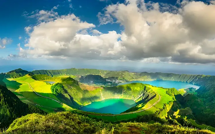 Panoramablick auf die Caldera mit grünen Hängen und türkisfarbenen Seen unter Wolken.