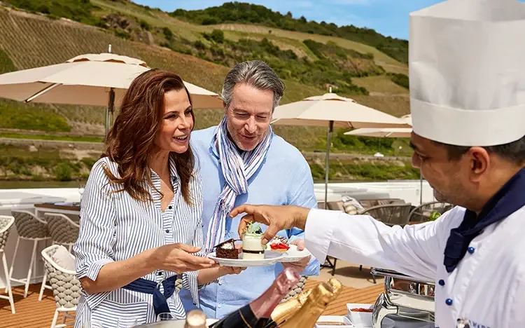 Paar genießt Desserts an Deck eines Flusskreuzfahrtschiffes mit Blick auf Weinhänge