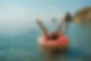 Person entspannt auf aufblasbarem Donut im Meer mit ausgestreckten Armen vor Küstenlandschaft