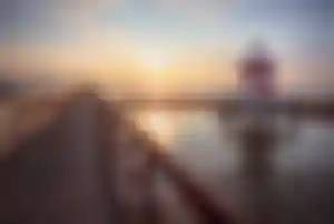 Langer Holzsteg mit rot-weißem Leuchtturm an der italienischen Adriaküste bei Sonnenaufgang über dem Meer.