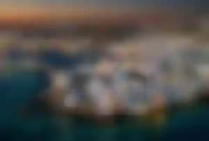 Luftaufnahme von Mykonos mit weißen Häusern, Hafen und Küstenlandschaft bei Sonnenuntergang