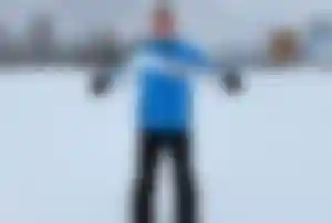 Person in Winterausrüstung auf verschneiter Piste mit umliegenden Bäumen und Berglandschaft