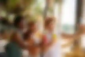 Drei Reisende machen gemeinsam ein Erinnerungsfoto mit Cocktails in einer Strandbar auf Mykonos